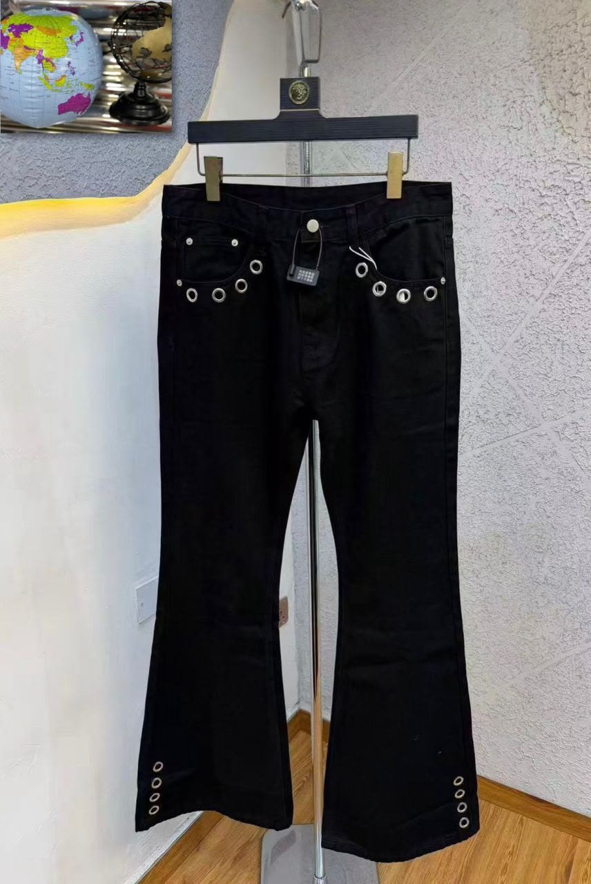 Front view of black baggy jeans with silver eyelets on pockets, waist and flared hems.