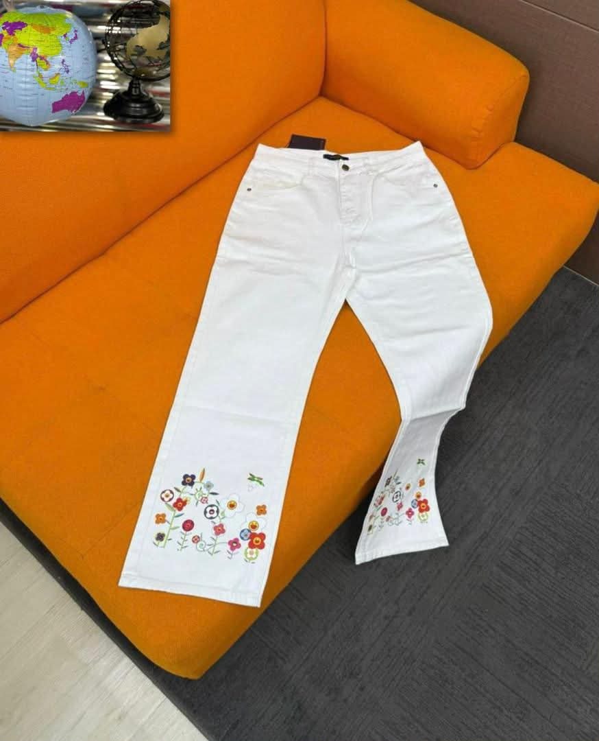 White baggy jeans with colorful floral and butterfly embroidery on the lower legs, laid on orange couch.