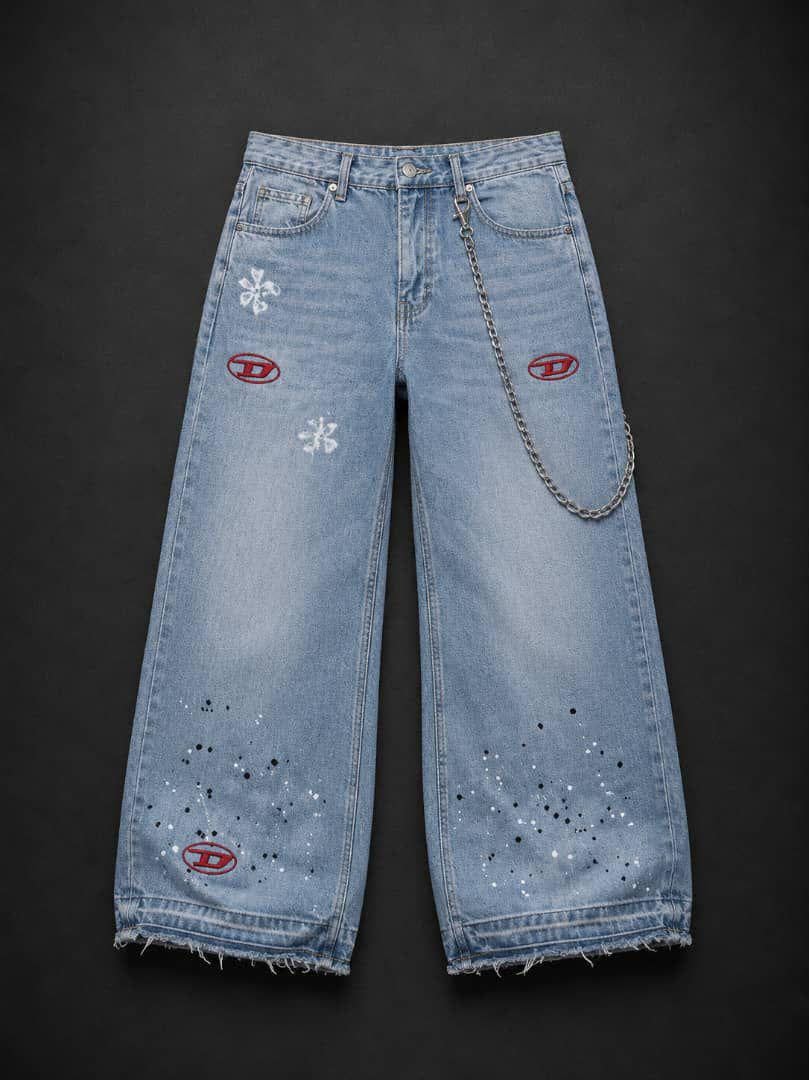 Flat lay of light blue baggy jeans with red embroidered logos, paint splatters, white patches and attached chain.