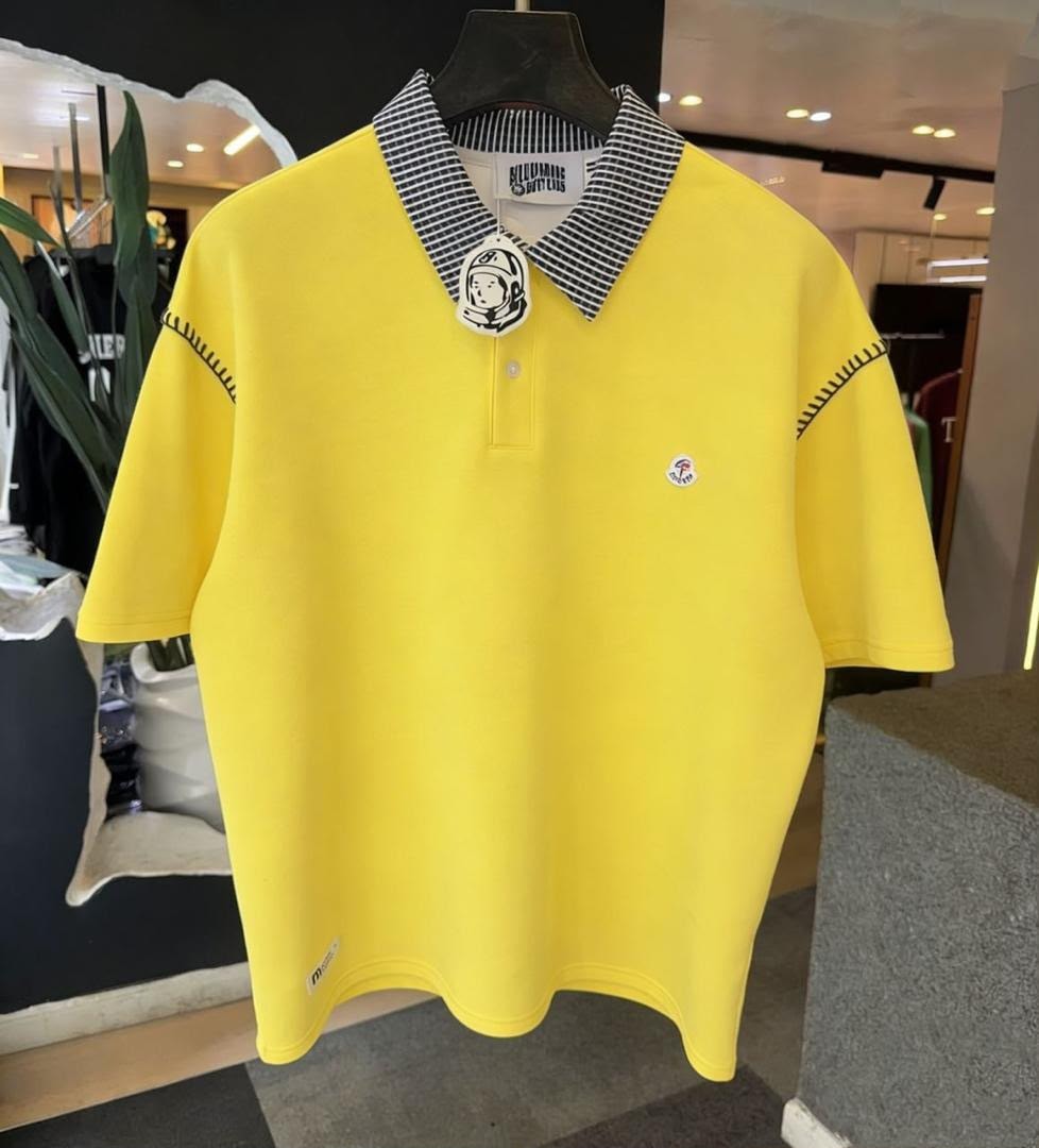 Yellow polo shirt hanging on mannequin in store, front view with striped collar and logo.
