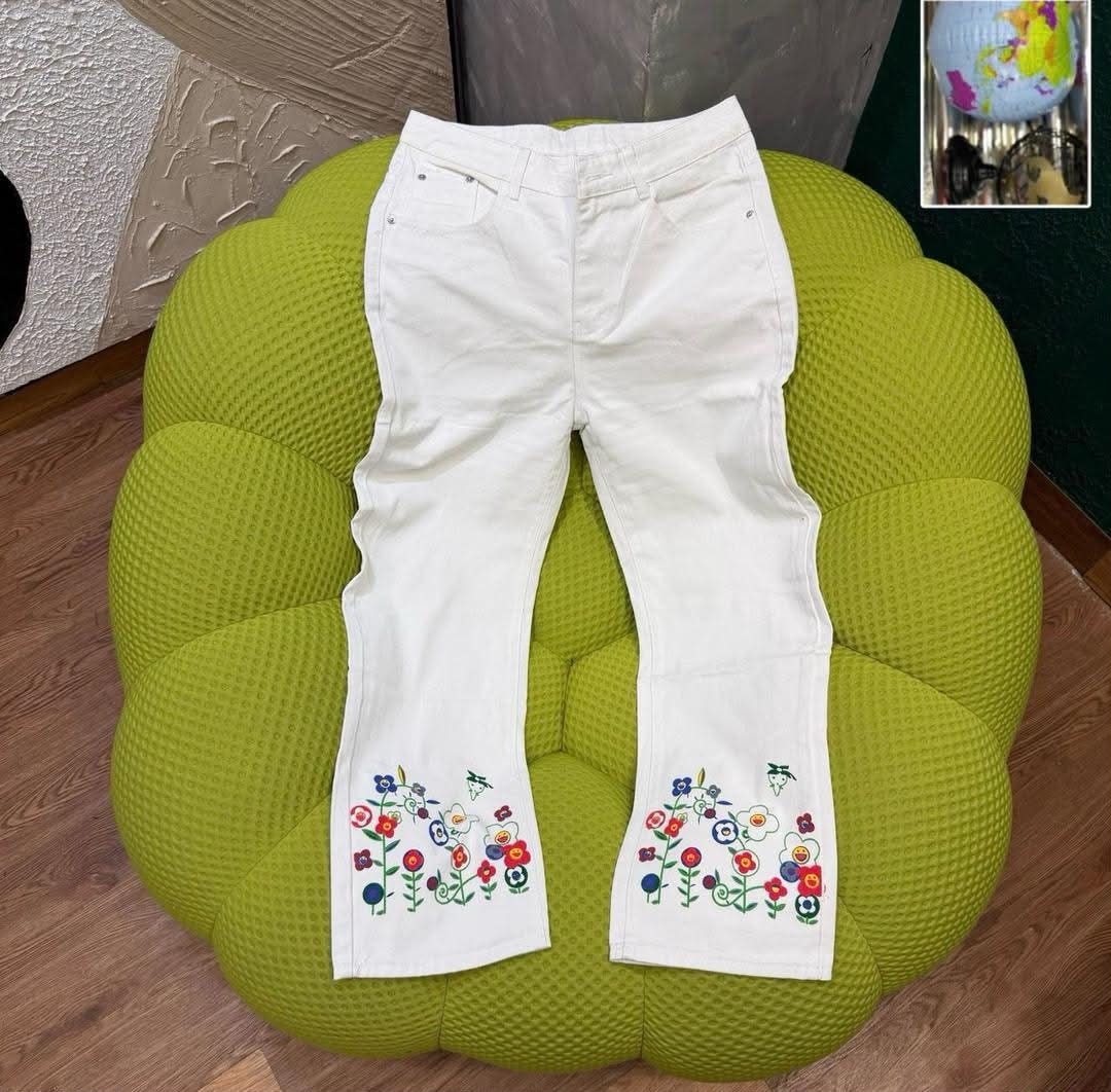White flared jeans with multicolored floral embroidery on legs placed on green ottoman.