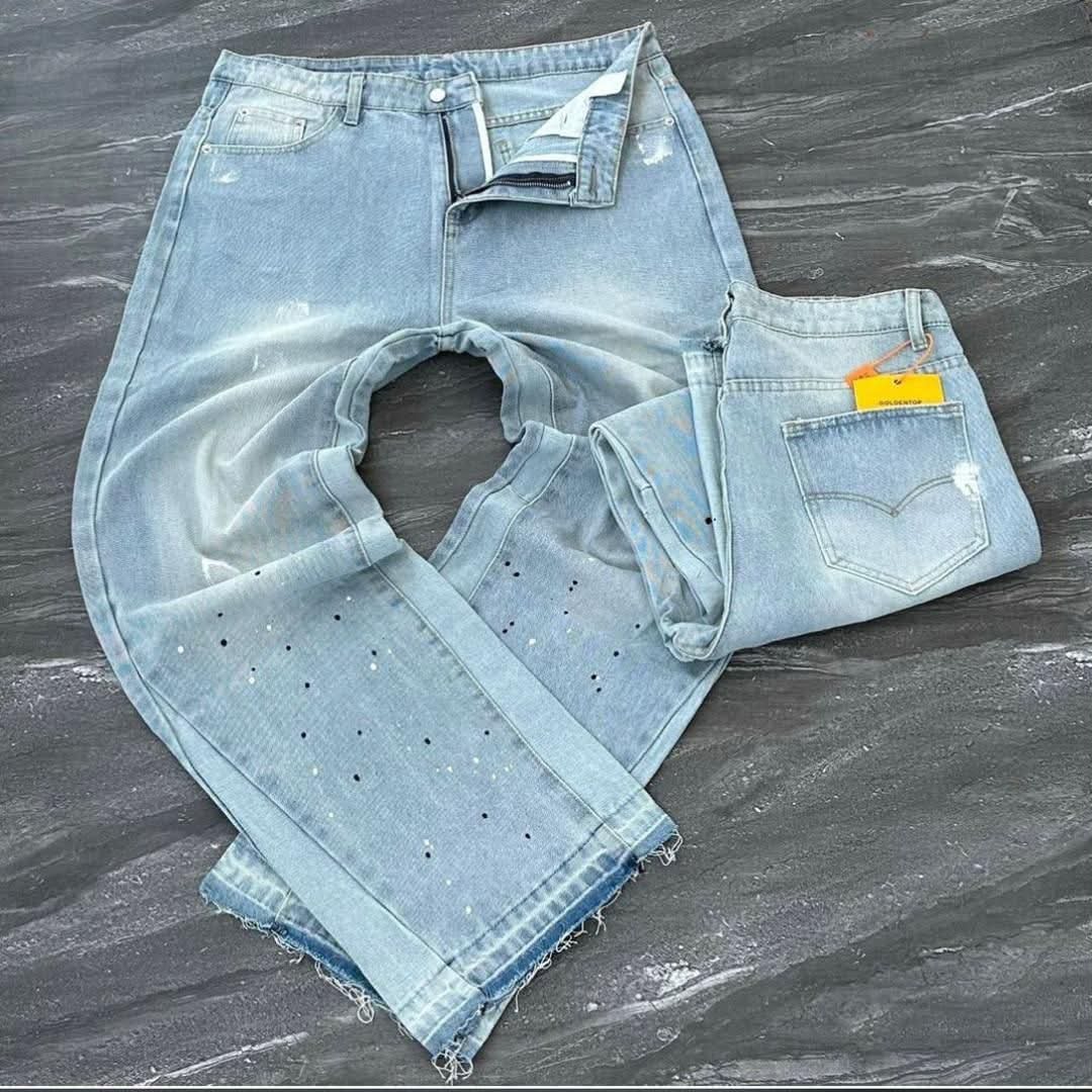 Light blue baggy jeans with multi-color splatter dots and frayed hems laid on dark surface.