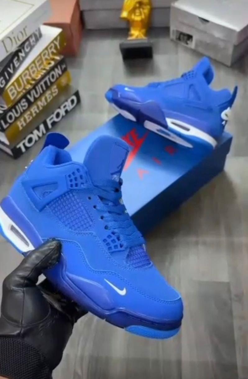 Blue Nike Air Jordan 4 sneaker held in hand with blue box and fashion books.