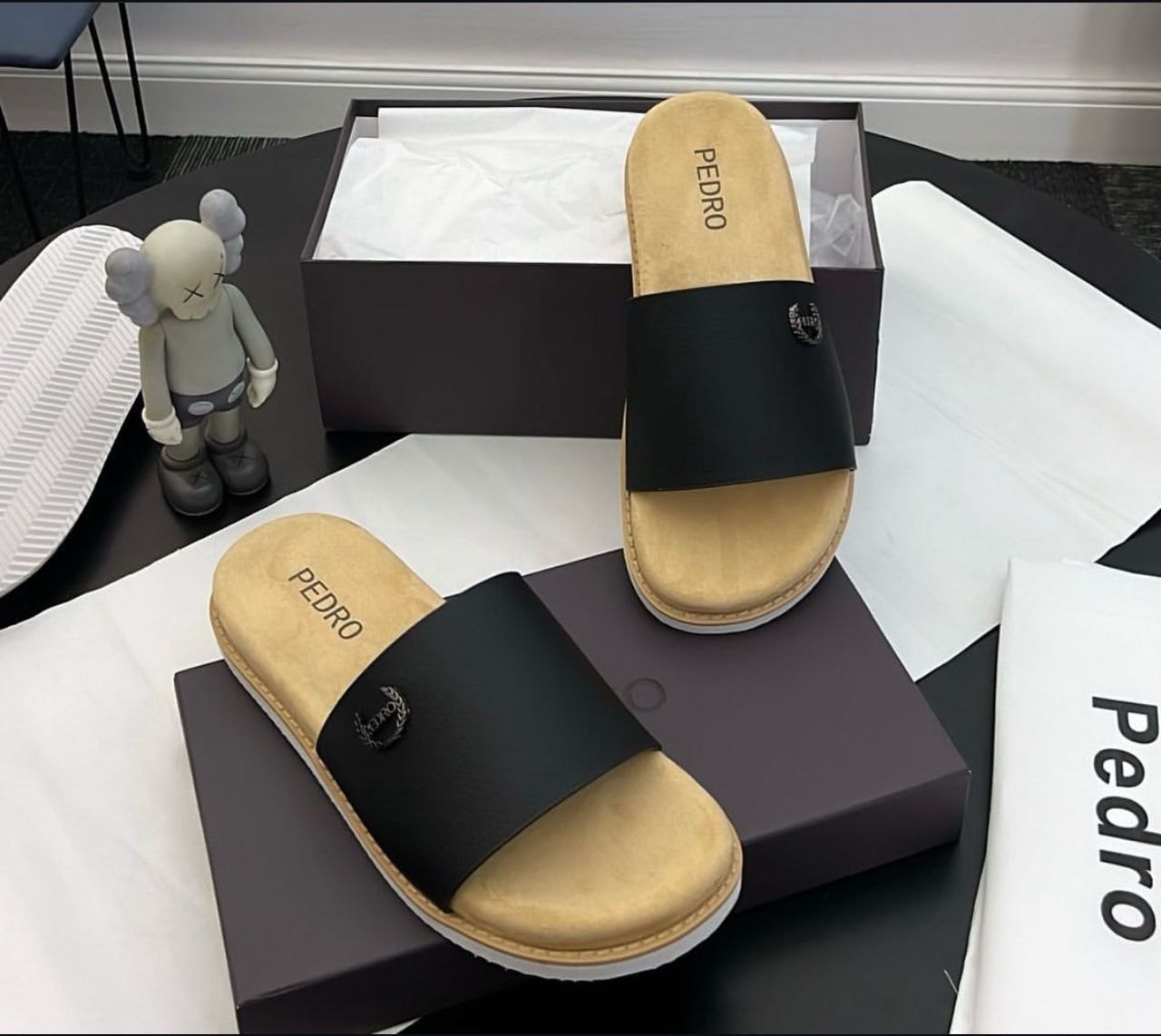 Black Pedro single-strap slide with logo, displayed with packaging, tissue and figurine.