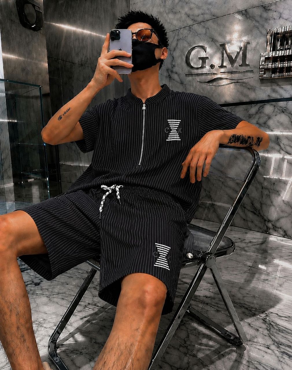 Man seated wearing black striped zip polo shirt and matching shorts with COK logo.