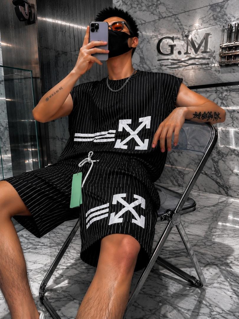 Man seated in black striped sleeveless top and matching shorts with large white arrow graphics.