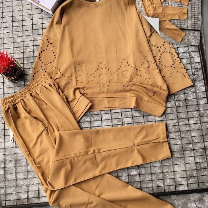Tan sweatshirt with eyelet cutout details and matching trousers laid on grid surface.