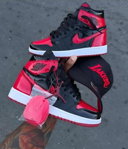 Red and black Jordan 1 high sneakers with red accessories and Lakers cap.