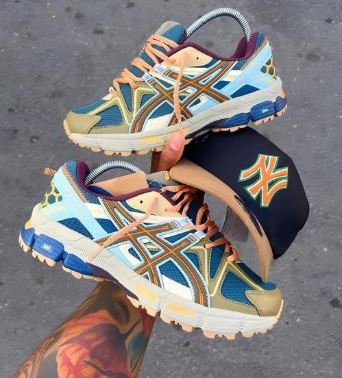 Multi-colored Asics sneakers in blue, brown and orange held with black NY cap.