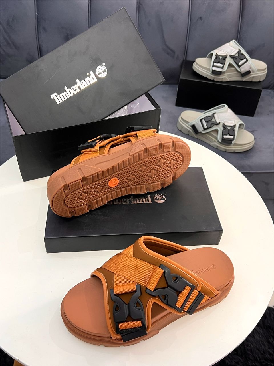 Timberland sandals shown in orange and gray colorways with boxes.