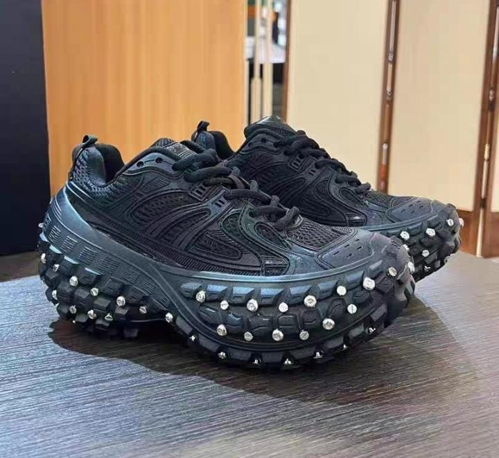 Black studded chunky sneakers on wooden surface.