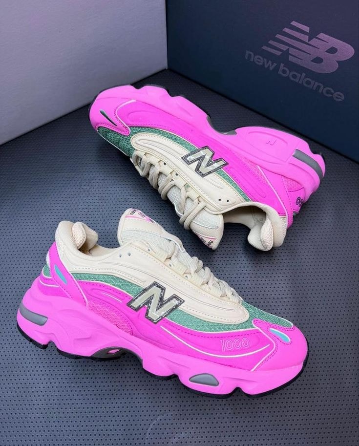 Pink New Balance 1000 sneakers with green and cream details on dark surface.