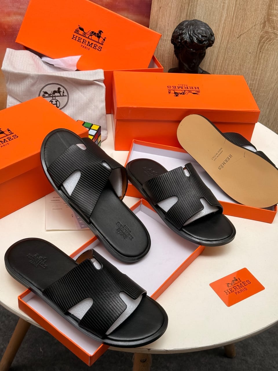 Black Hermes ribbed strap H slides with packaging and accessories on display.