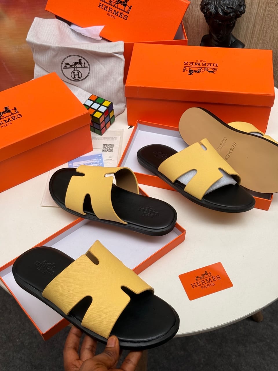 Yellow Hermes H-strap slides with black sole displayed with branded packaging.