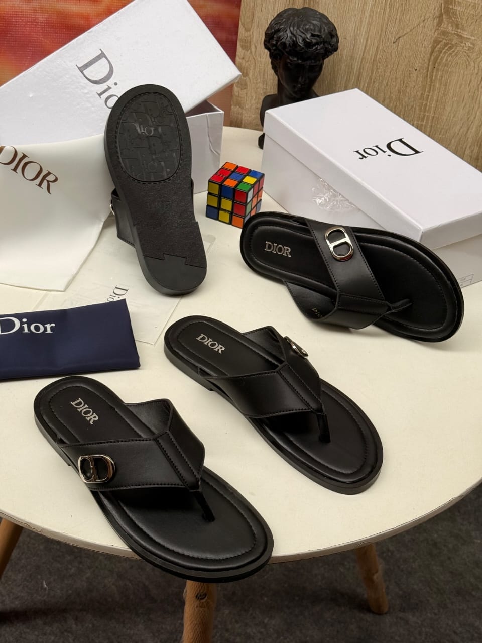 Black Dior thong slides with gold D buckle and branded soles with white boxes.
