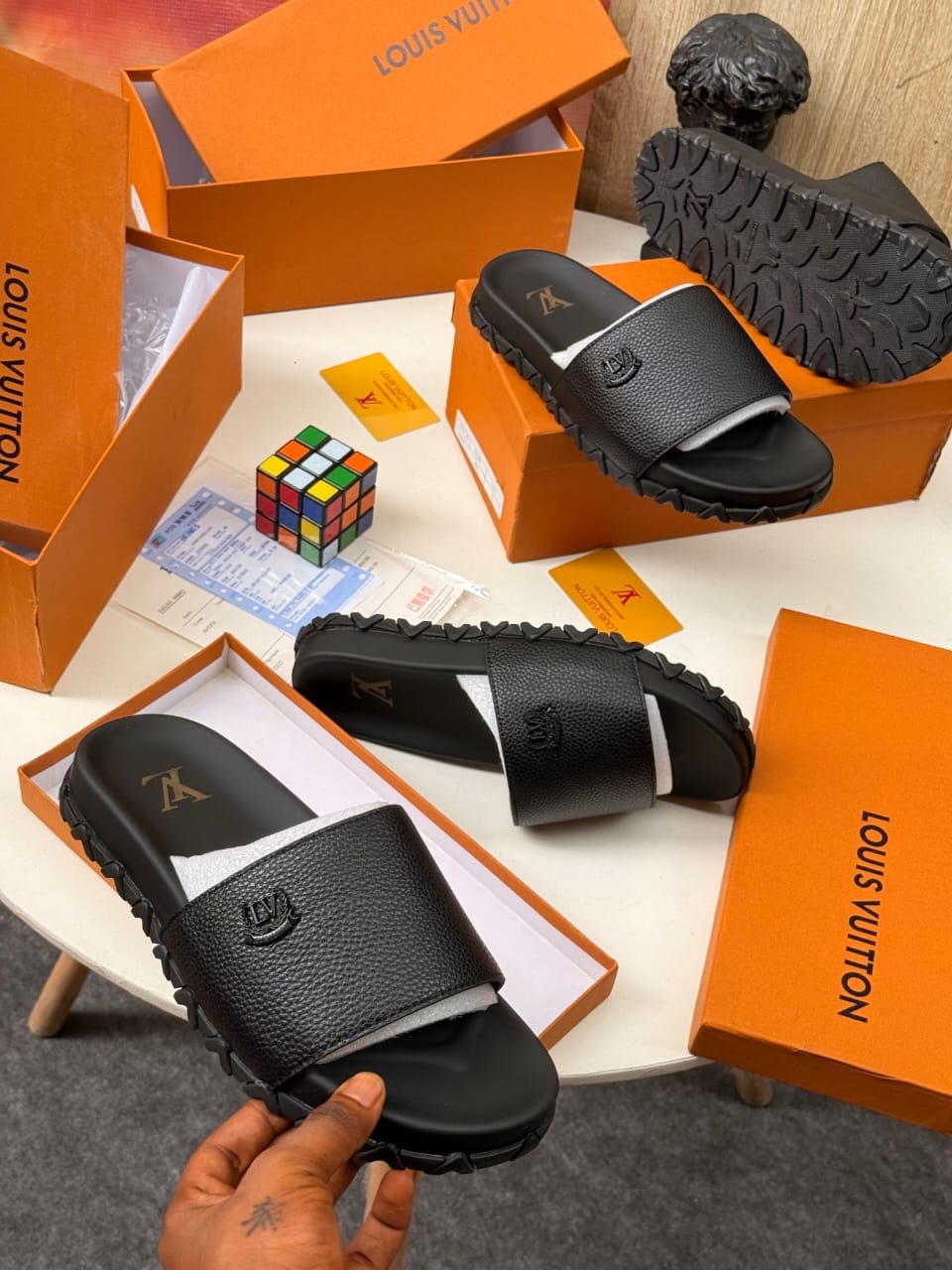 Black Louis Vuitton slides with embossed logo and chunky tread sole shown with orange boxes.
