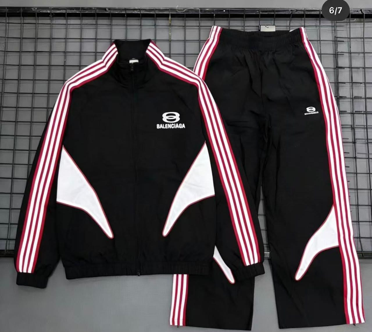 Black Balenciaga tracksuit with red and white stripes laid flat on a grid background.