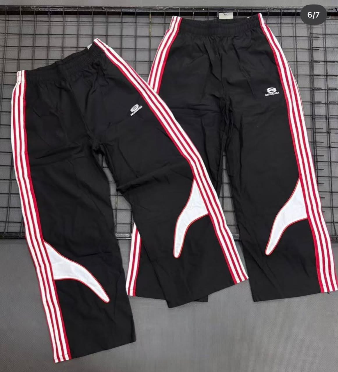 Two black track pants with red and white side stripes and Balenciaga logo.