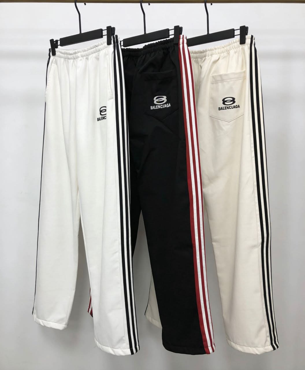 Three track pants in white, black, and cream with side stripes and Balenciaga logo.