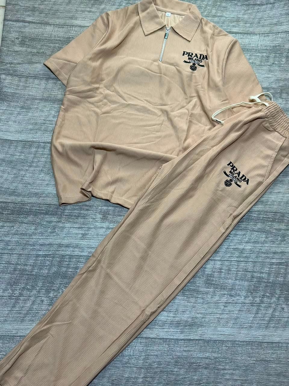 Beige ribbed polo shirt and jogger pants two-piece set laid flat on wood floor.