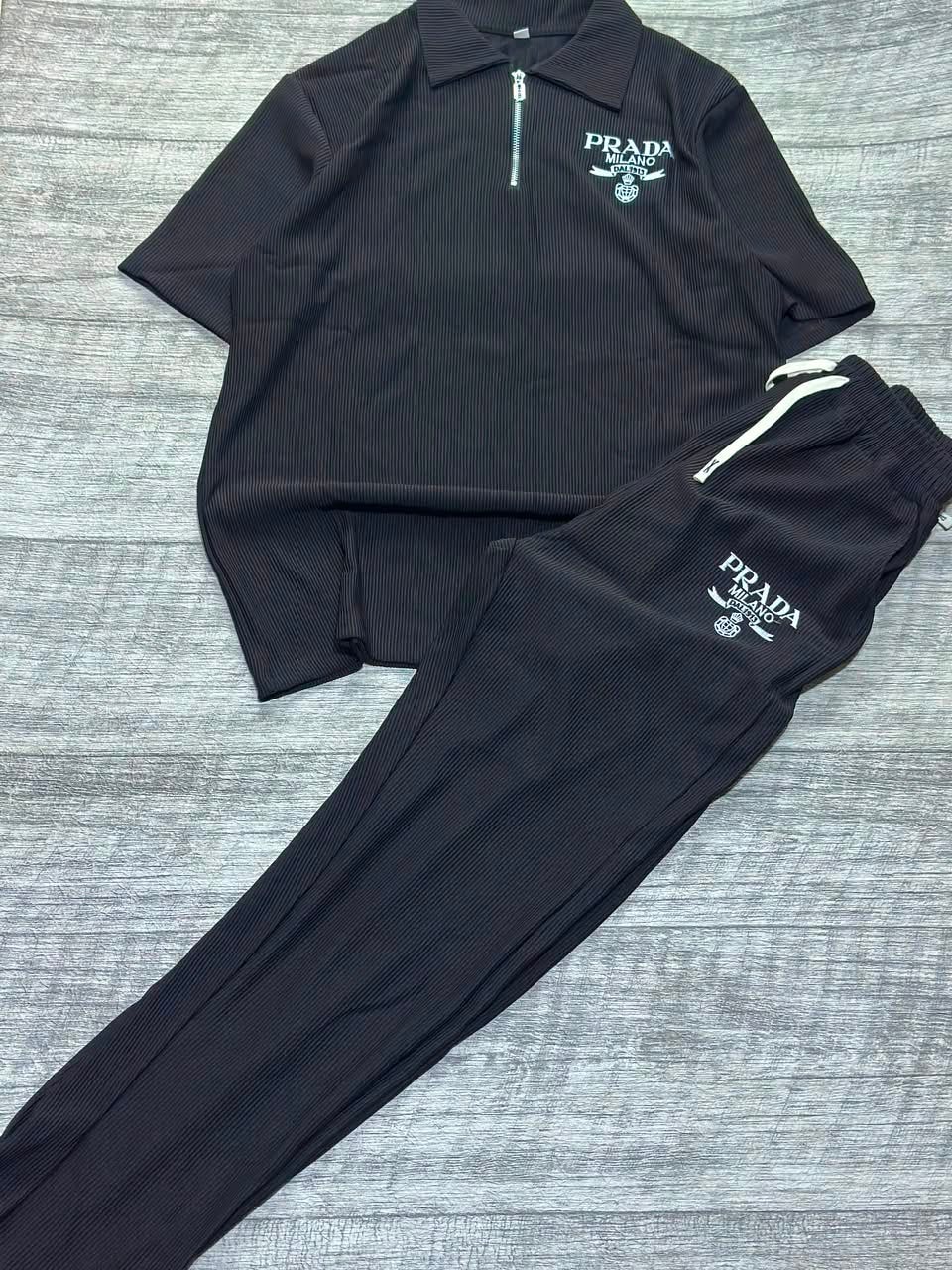 Black ribbed polo shirt and jogger pants two-piece set laid flat on wood floor.