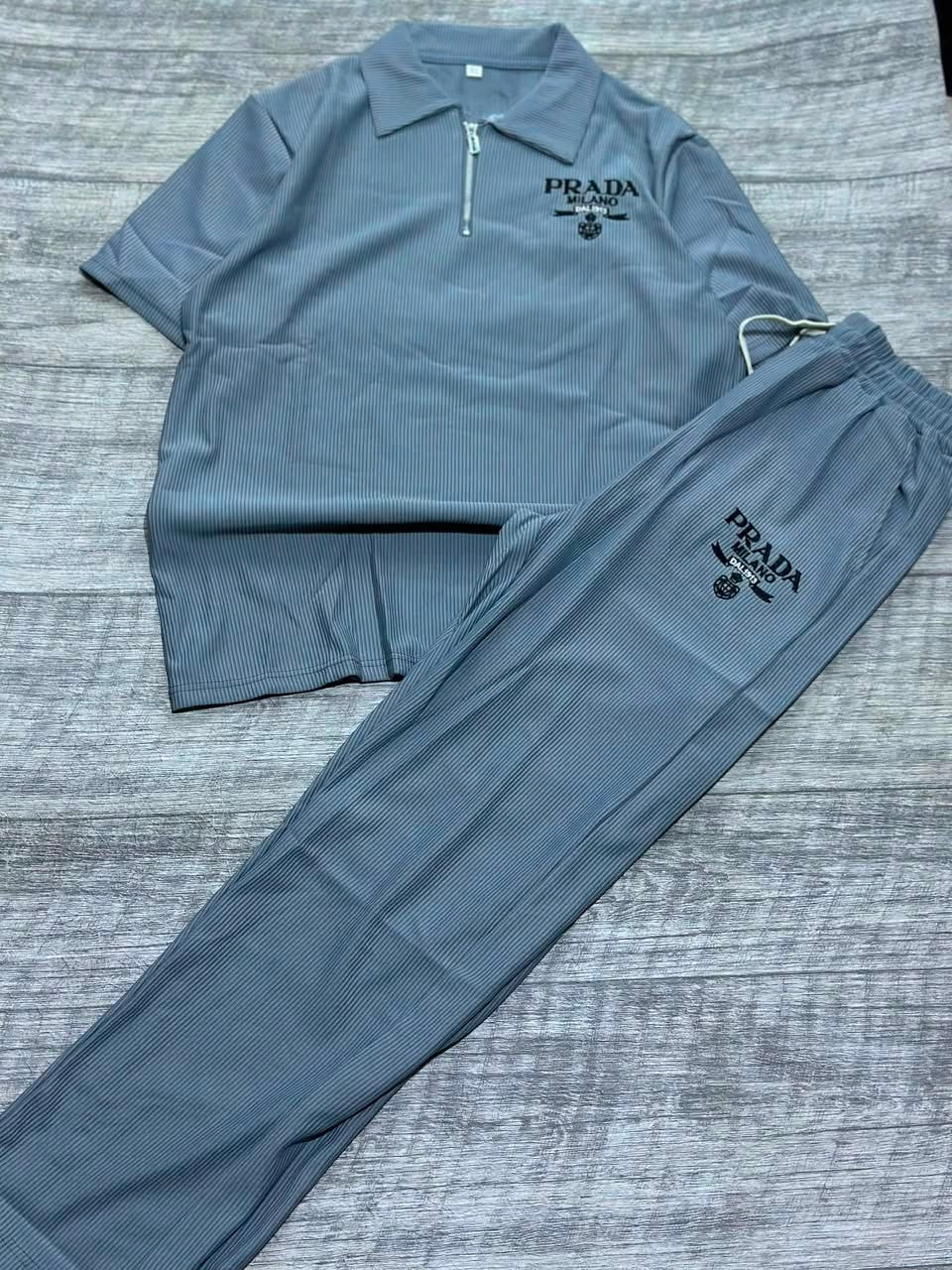 Gray ribbed polo shirt and jogger pants two-piece set laid flat on wood floor.