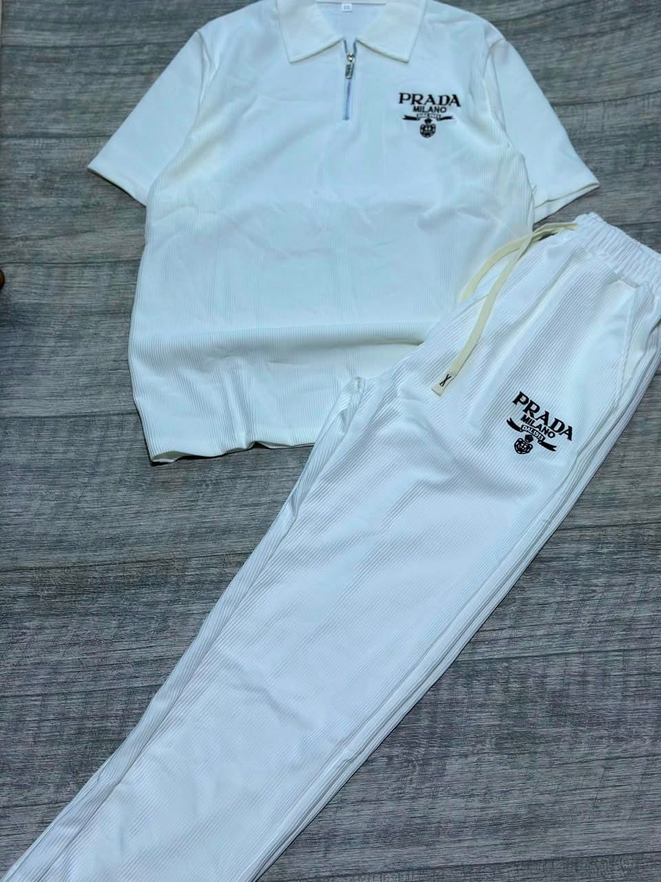 White ribbed polo shirt and jogger pants two-piece set laid flat on wood floor.