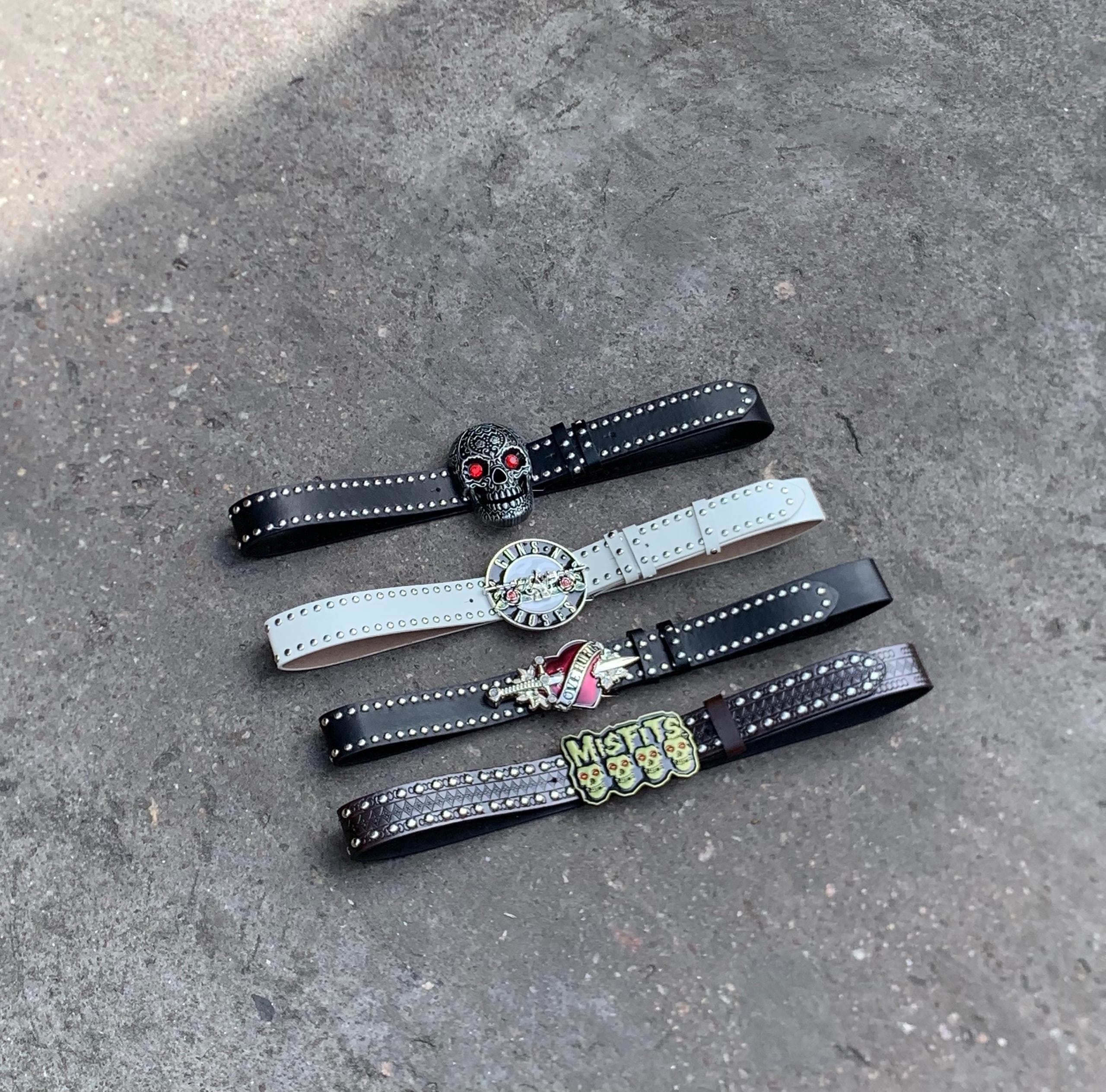 Four rock themed studded belts with various skull buckles laid out.