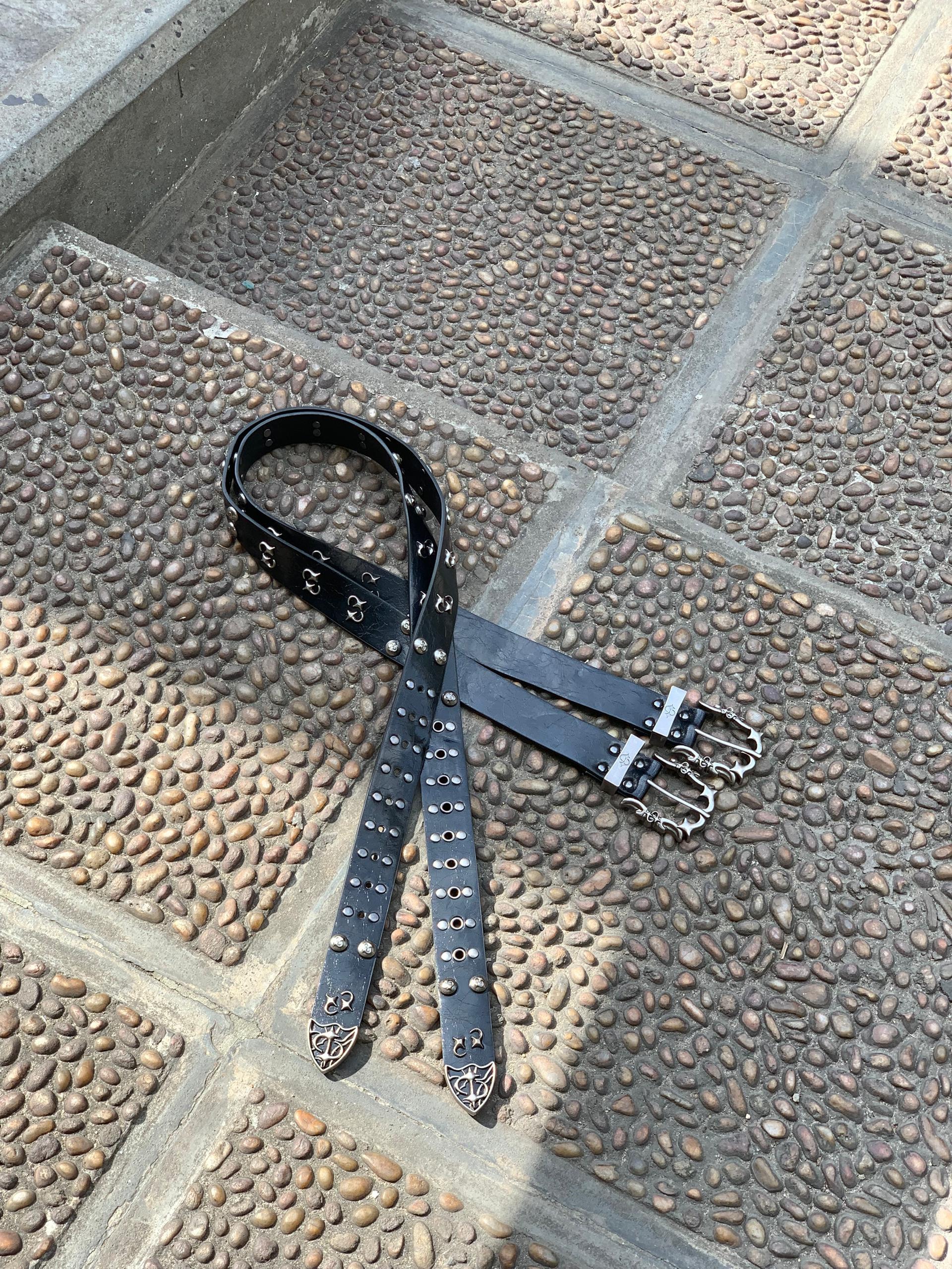 Black belt with silver cross and skull designs on cobblestone floor.