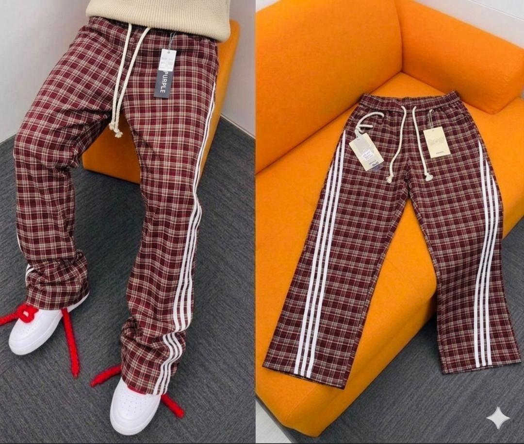 Burgundy plaid pants with white side stripes laid flat on an orange couch, showing drawstring waist and tags.