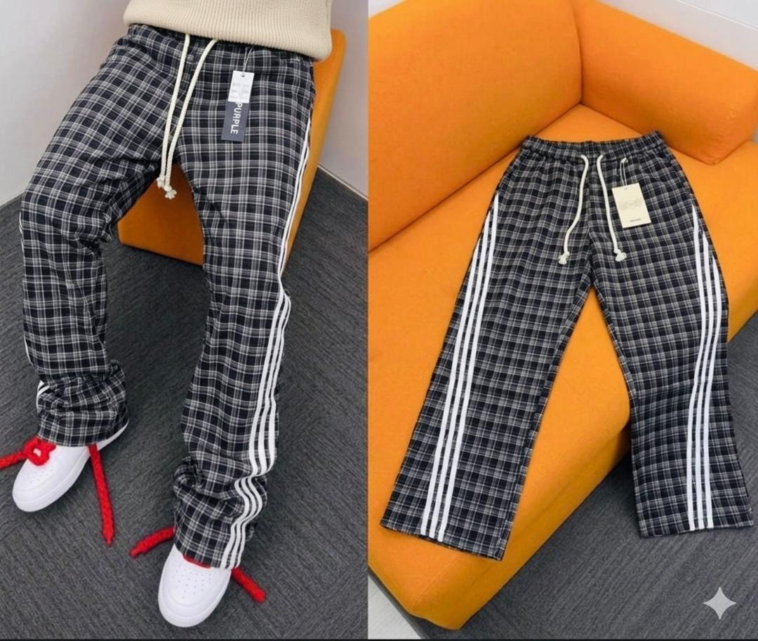 Model wearing black plaid pants with white side stripes, paired with a beige sweater and white sneakers.
