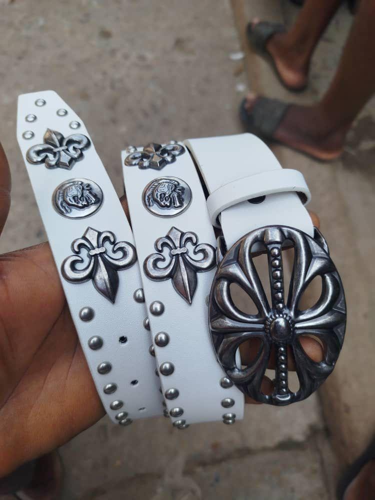 Close-up of white leather designer belt with silver fleur-de-lis, lion emblem and ornate buckle.