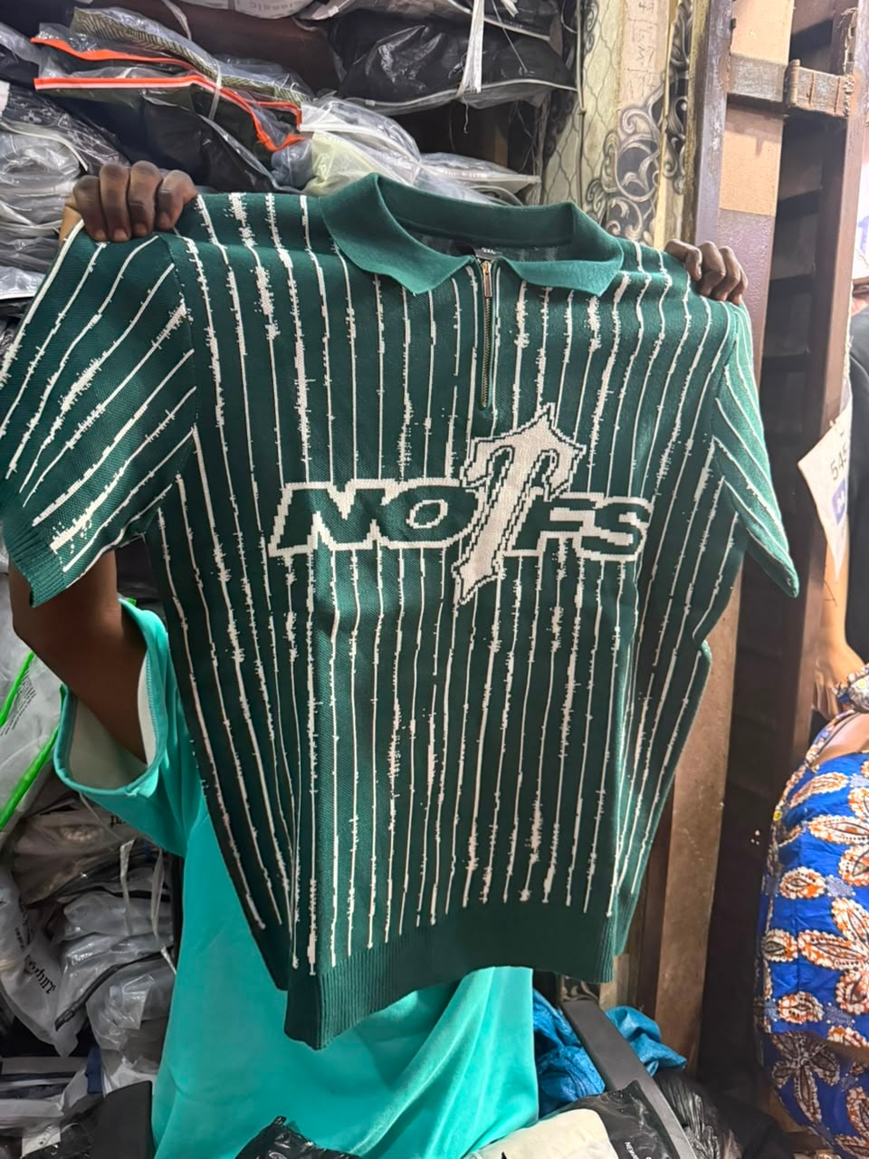 Green vertical striped NO1FS knit polo with white graphic held by hands.