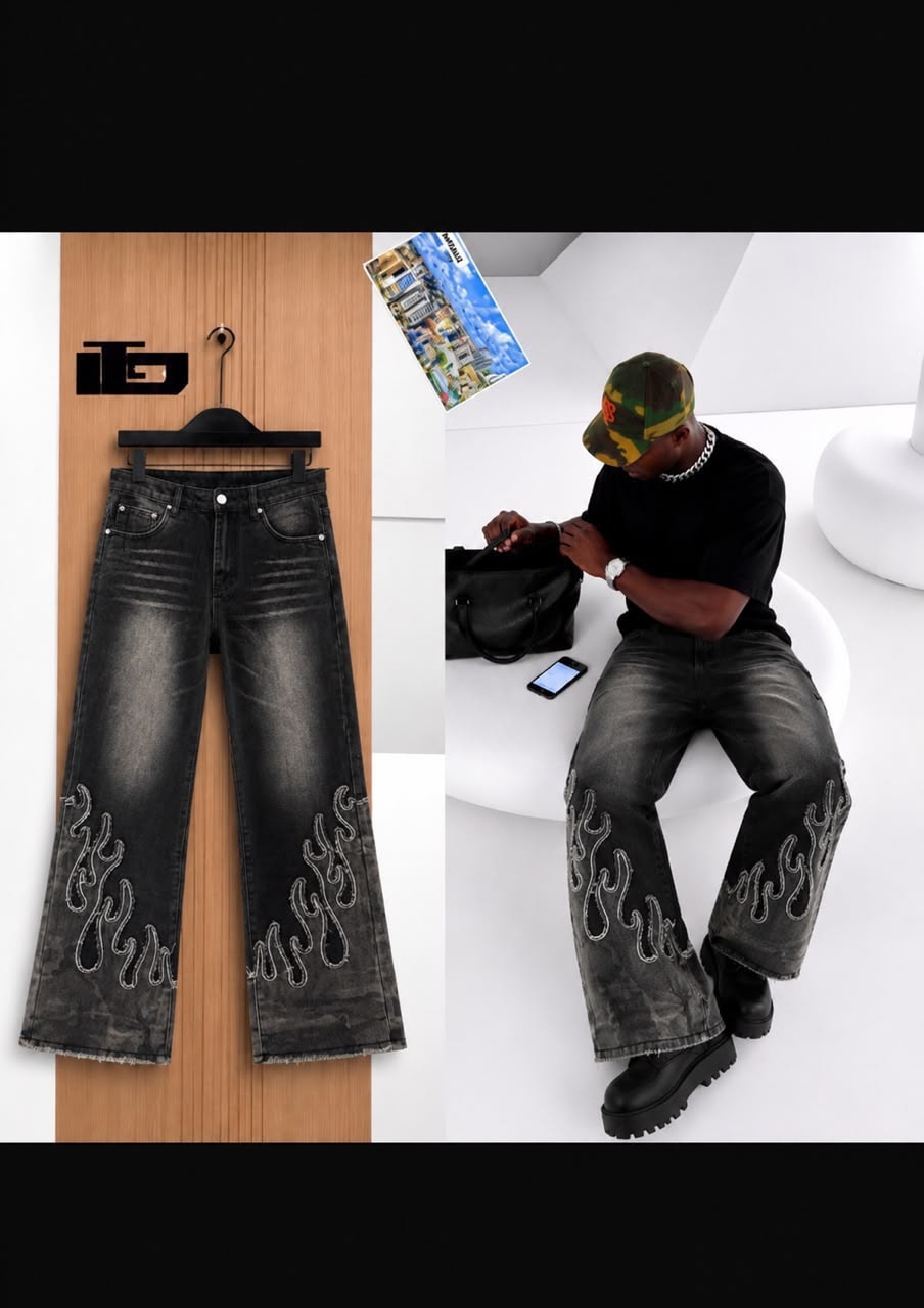 Black baggy jeans with white flame embroidery shown on hanger and worn by model in modern studio.