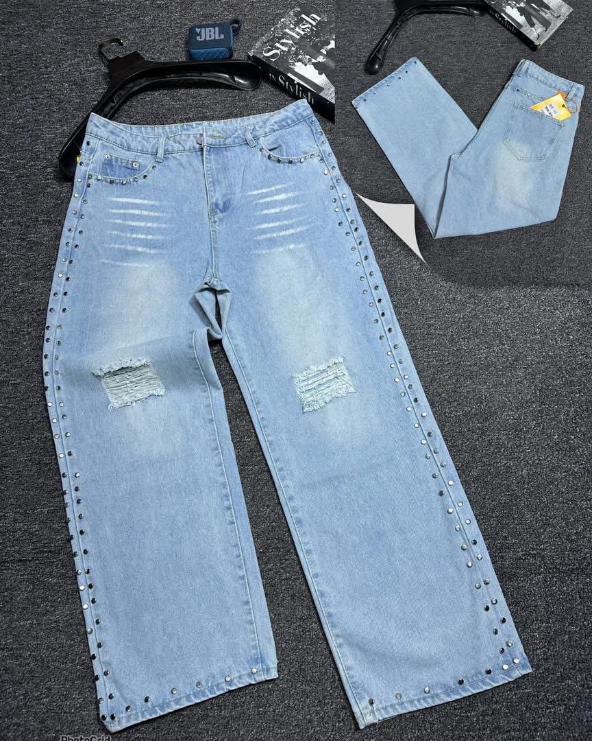 Flat lay of light blue baggy jeans with rips, studs on seams and pockets.