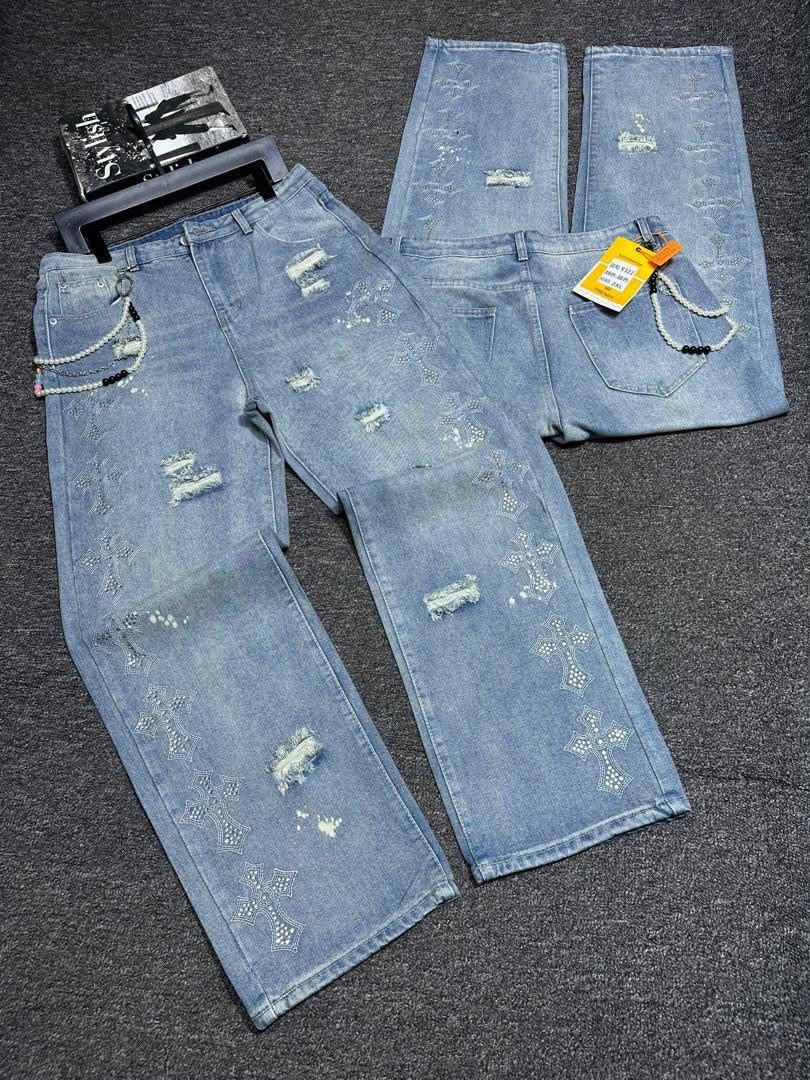 Flat lay of light blue distressed baggy jeans with cross patterns and accessories.