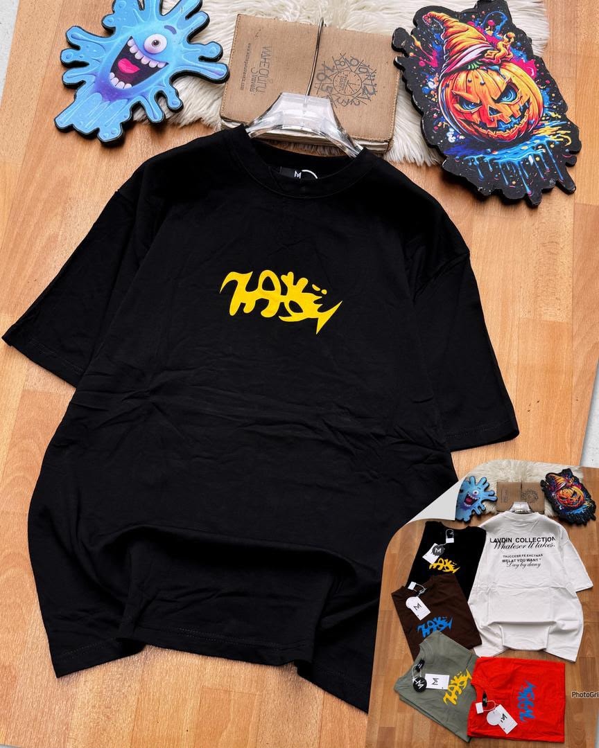 Black oversized t-shirt with yellow chest graphic on wooden surface alongside props and smaller images of other variants.