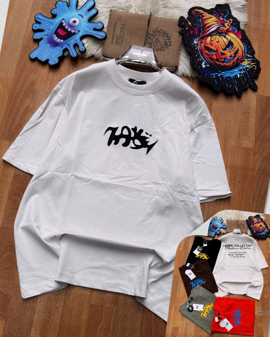 White oversized t-shirt with black chest graphic, shown flat with decorative elements and inset of multiple color options.