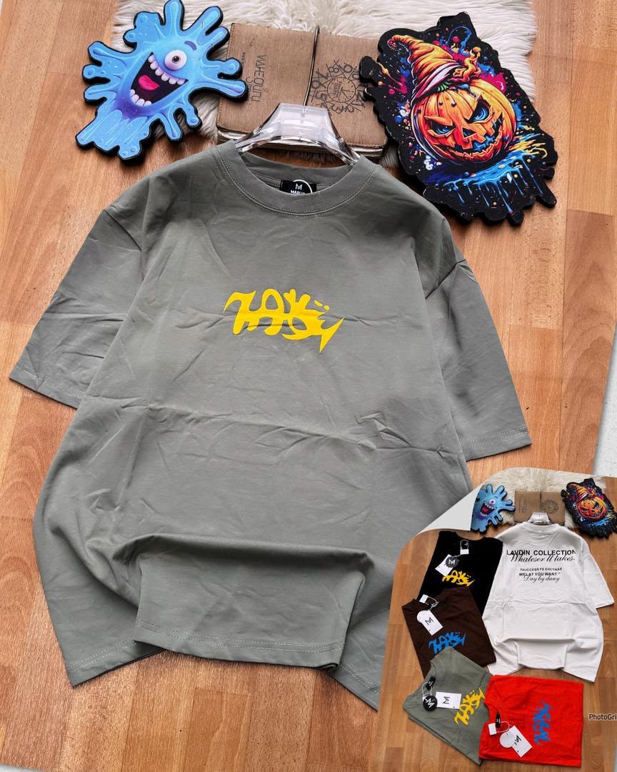 Gray oversized t-shirt with yellow chest graphic, laid flat with props and inset of other colors.