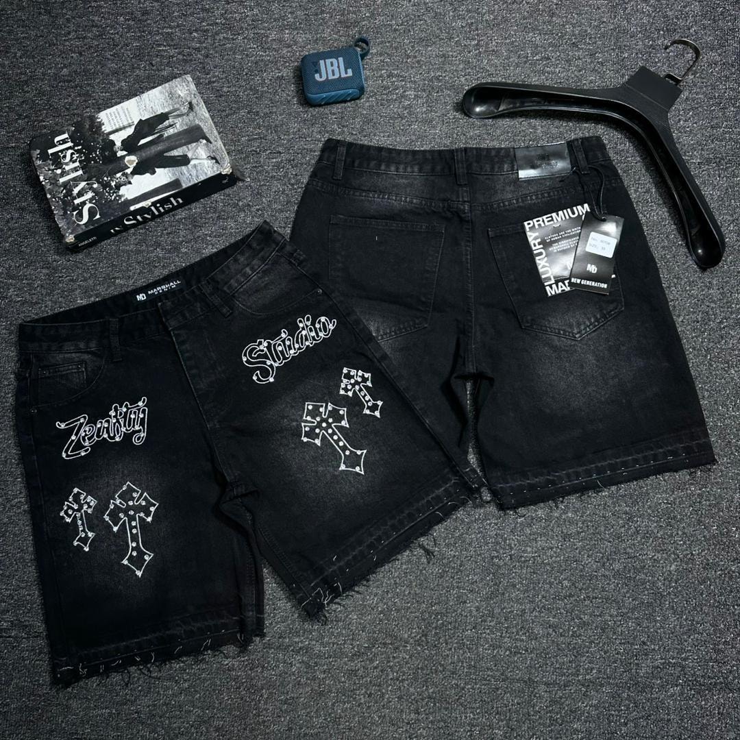 Flat lay of black baggy denim shorts with white embroidery designs, Zenith script with crosses on one and Studio on the other, including back view with tags.