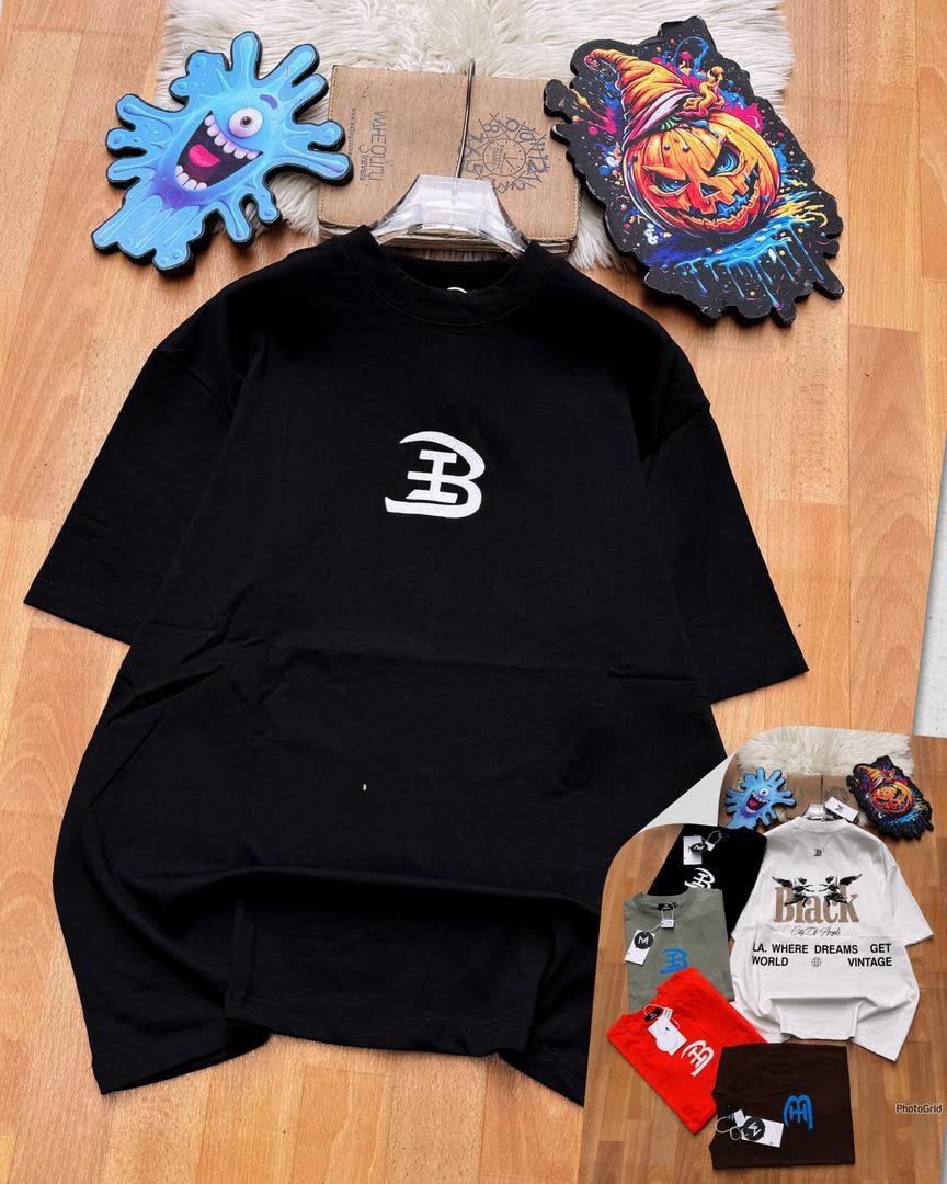 Black oversized t-shirt with white B logo on chest laid on wooden floor with accessories.