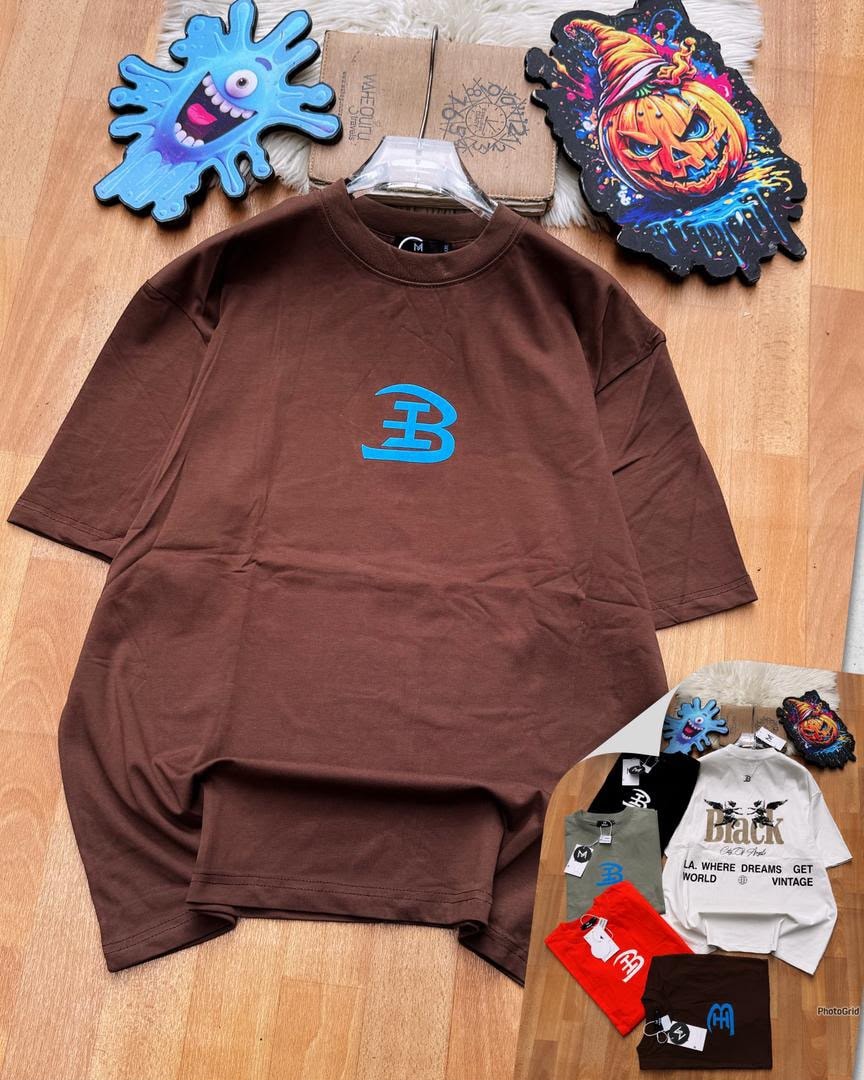 Brown oversized t-shirt with blue B logo on chest laid on wooden floor with accessories.