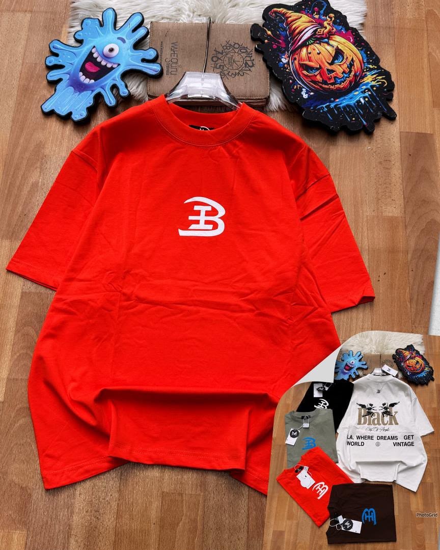 Red oversized t-shirt with white B logo on chest laid on wooden floor with accessories.