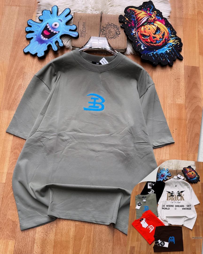 Olive oversized t-shirt with blue B logo on chest laid on wooden floor with accessories.