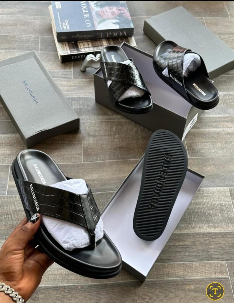 Black Balenciaga croc embossed flip flops held in hand with box and another style visible.