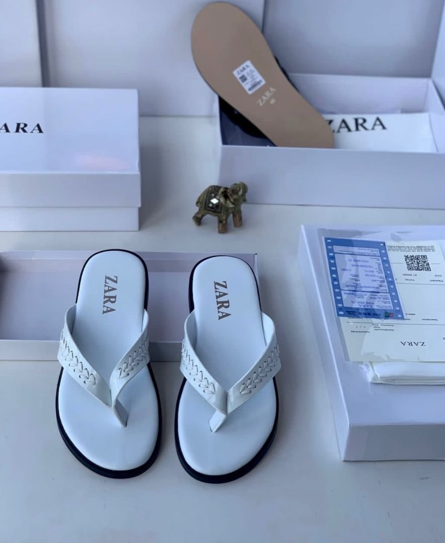 White Zara flip flops with braided straps displayed with boxes and accessories.