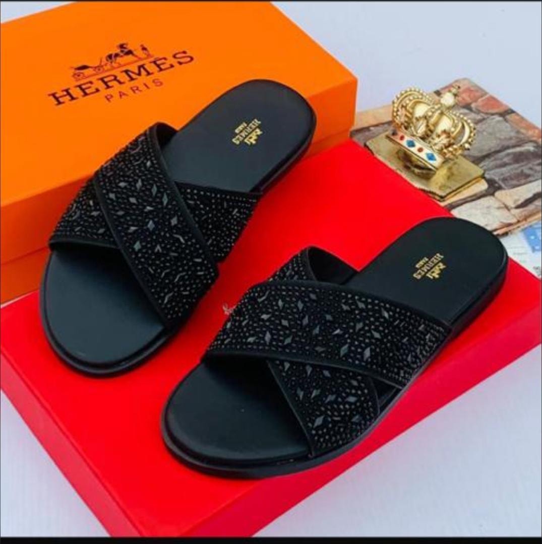Black cross-strap slides with rhinestones on red box with Hermes packaging and crown accessory.