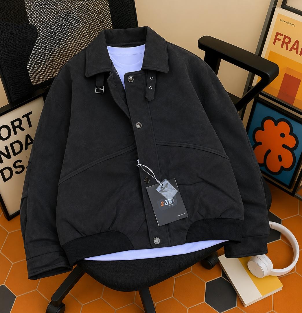 Black suede-like button-front bomber jacket with collar and tag detail, displayed on a chair.