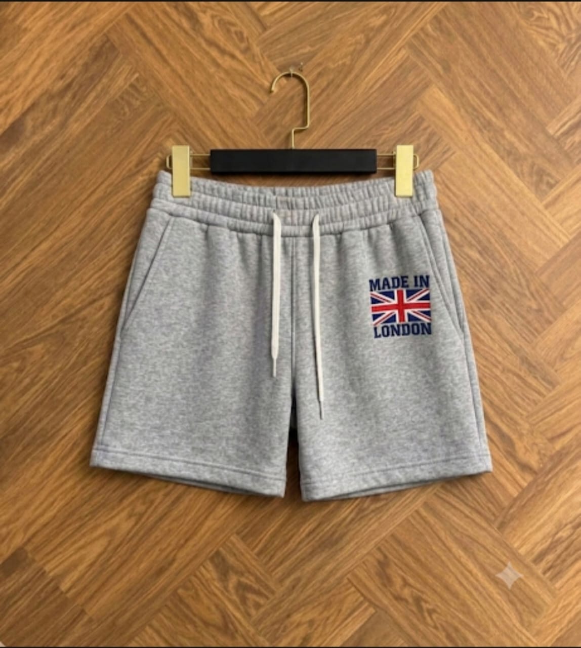 Gray fleece shorts with drawstring waist and Made in London embroidery on wooden floor.