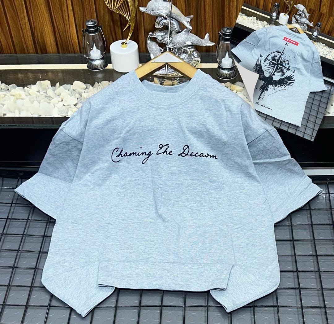 Light blue oversized t-shirt with black cursive 'Chaming The Decaom' print on front and inset bird compass back view.